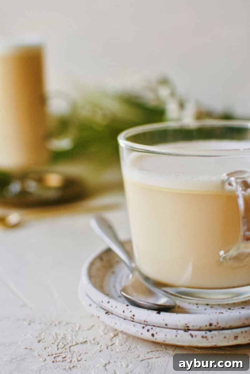 A close-up of a hot buttered rum in a mug, with a spoon resting on a small plate.