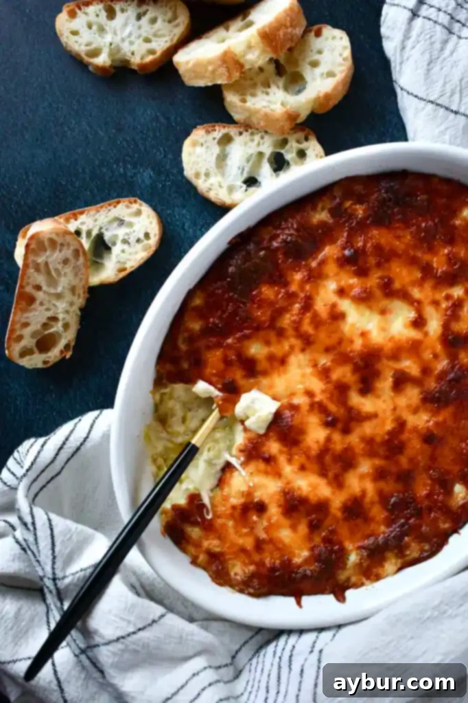 A large ceramic dish filled with Artichoke Three Cheese Dip, garnished with fresh herbs, ready for serving.