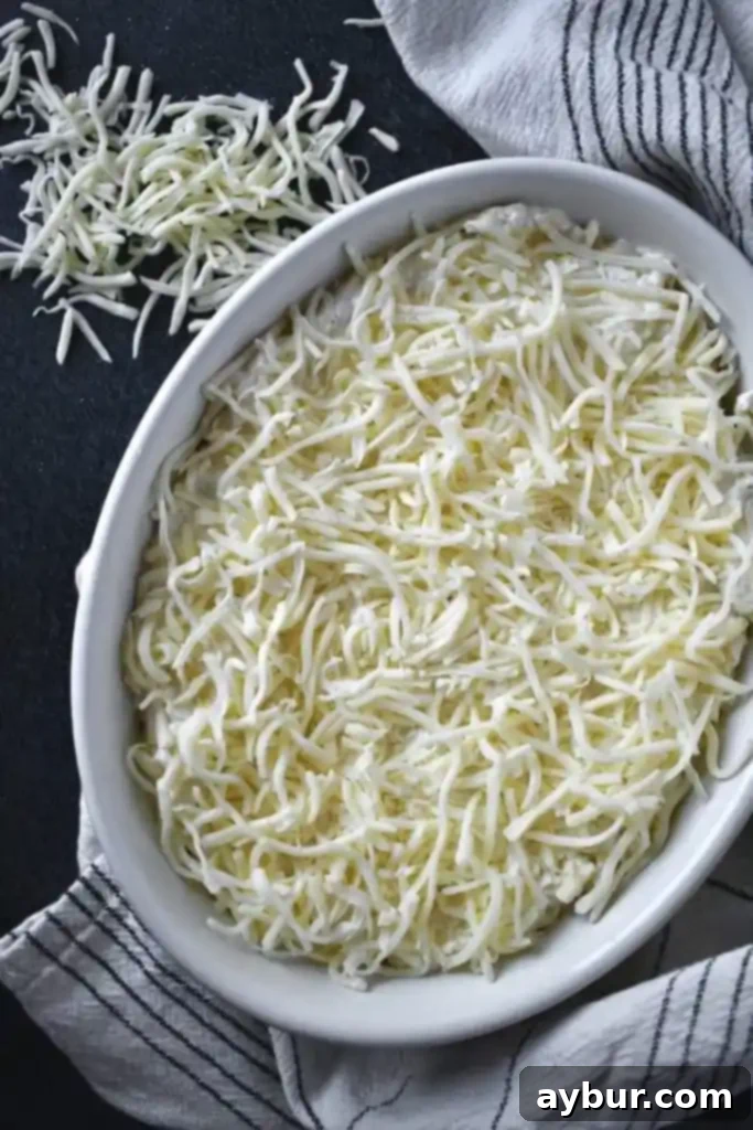 The Artichoke Three Cheese Dip mixture spread evenly in a baking dish, ready for the oven.