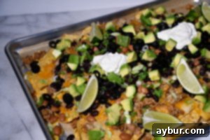 Perfect Movie Night Sheet Pan Nachos 3 Hand reaching for a nacho with a generous topping of avocado and lime