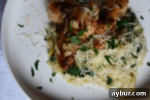 Plated almond crusted chicken tenderloins with a side of creamy risotto, garnished with herbs.
