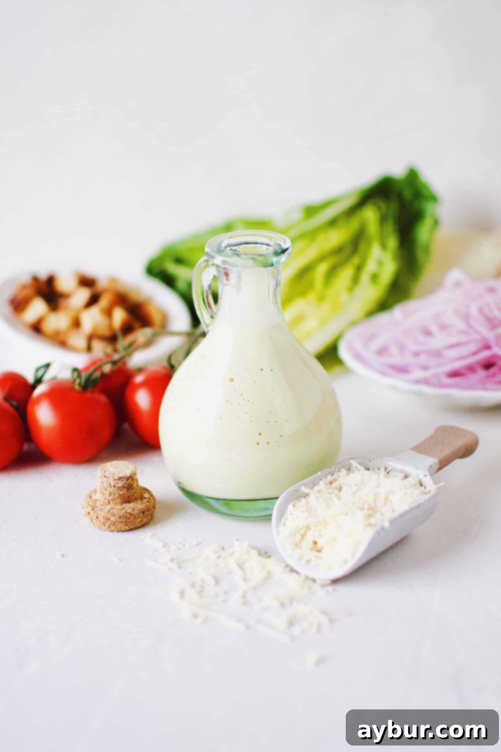 Velvety Caesar Dressing 3 Creamy Caesar Dressing in a bottle surrounded by ingredients needed to make a Caesar Salad.