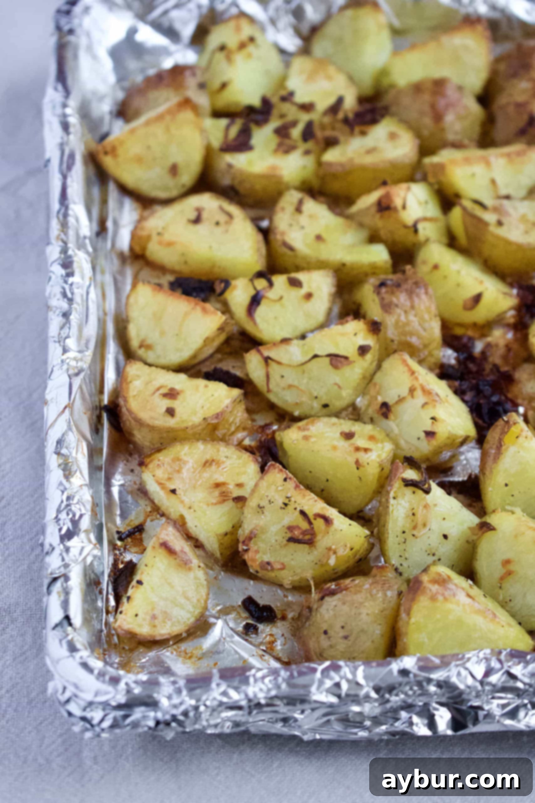 Golden Herb Roasted Potato Salad 4 Golden-brown roasted potatoes with caramelized shallots and garlic on a baking sheet.