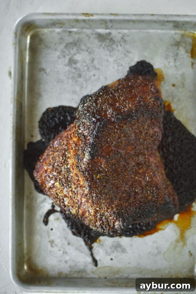 The finished corned beef brisket, beautifully glazed and crisped after baking in the oven, showcasing a dark, caramelized crust.