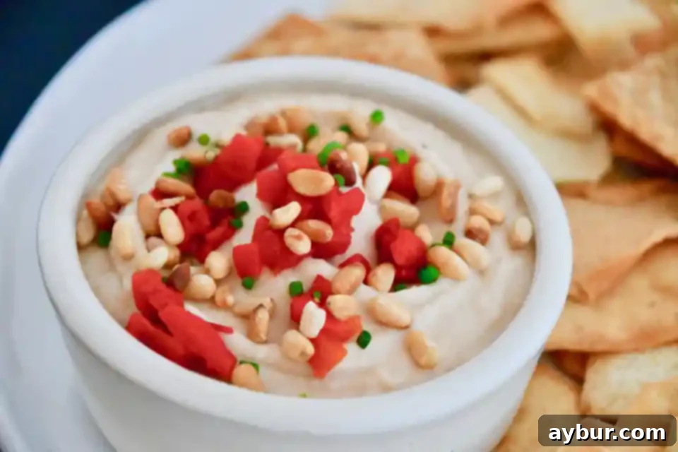 Close-up of creamy white bean hummus garnished with pine nuts and herbs