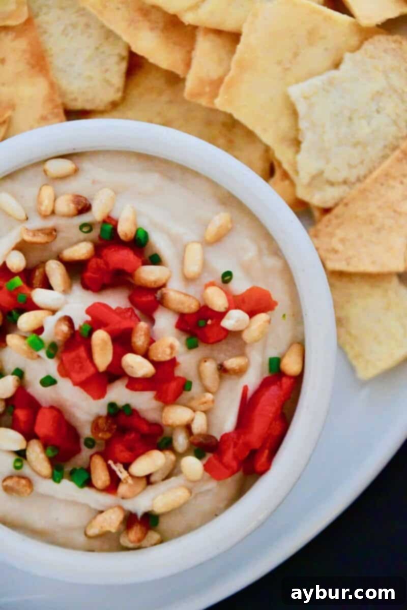 Joanna Gaines White Bean Hummus in a bowl topped with extra pine nuts and red peppers.