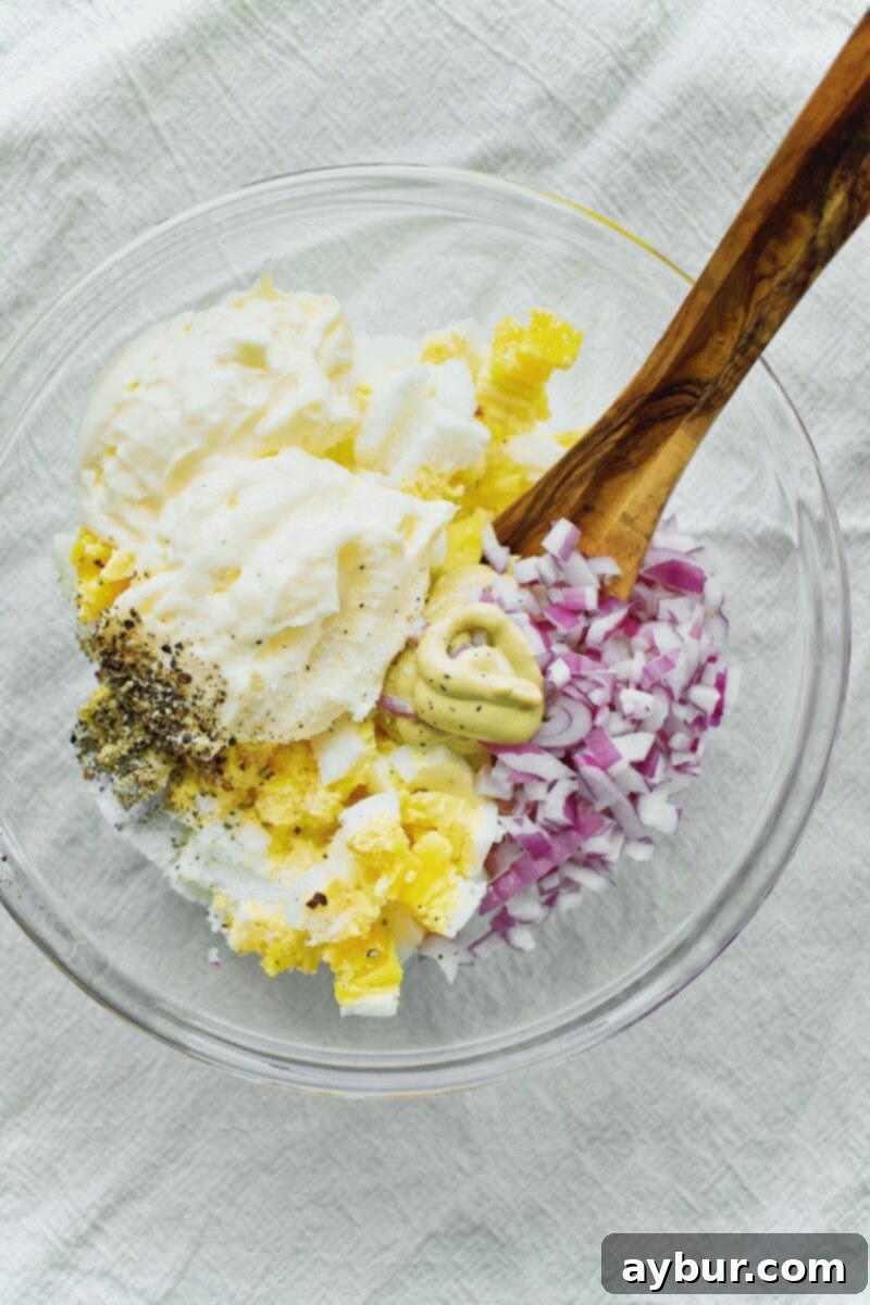 Scandinavian Dill Egg Salad 3 Egg Salad ingredients in a bowl before mixing, showcasing boiled eggs, diced red onion, and mayonnaise.