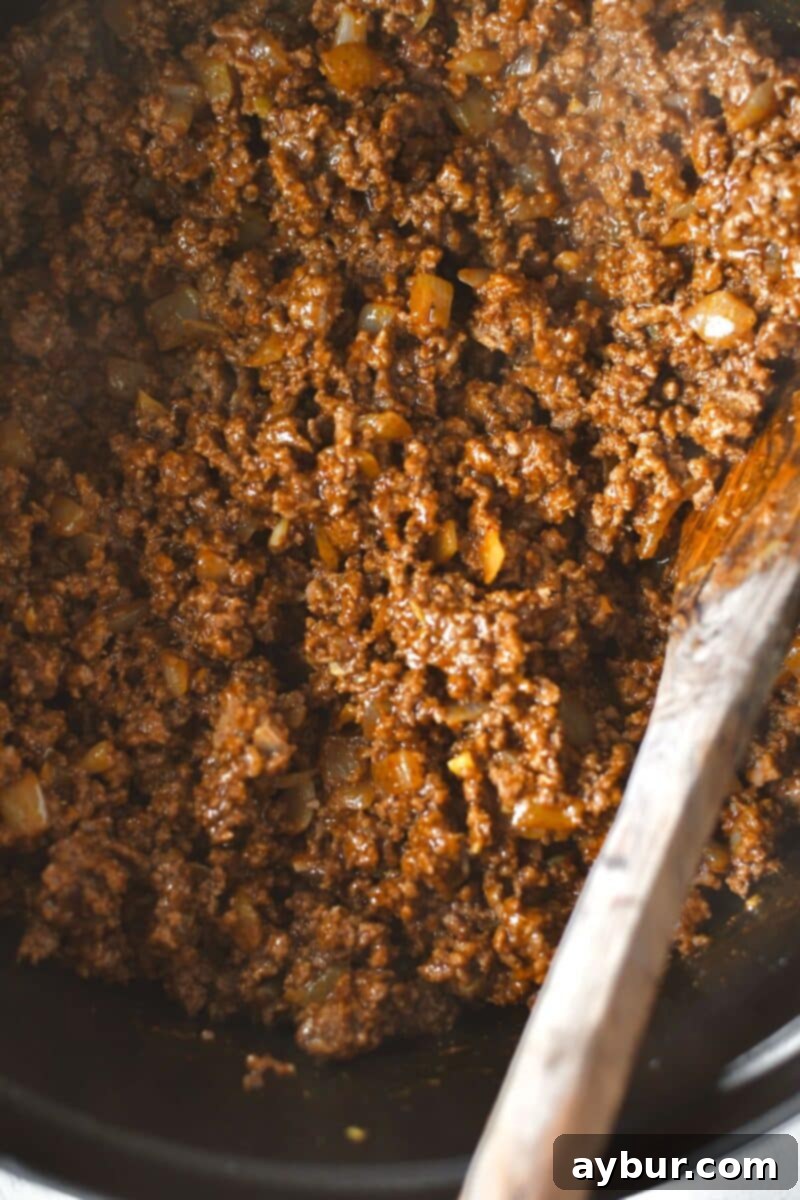 Adding and blooming the wet ingredients and beans into the browned meat mixture.