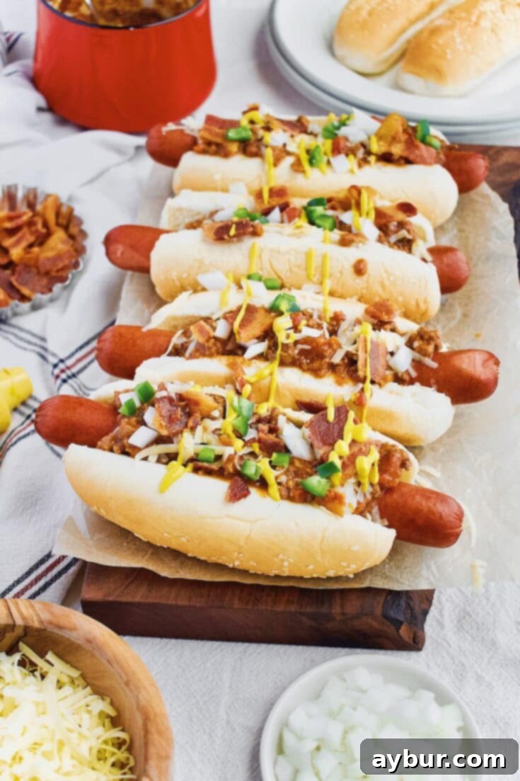 Ultimate Homemade Chili Dog Sauce topped on hot dogs with cheese, onions, jalapenos, and mustard.
