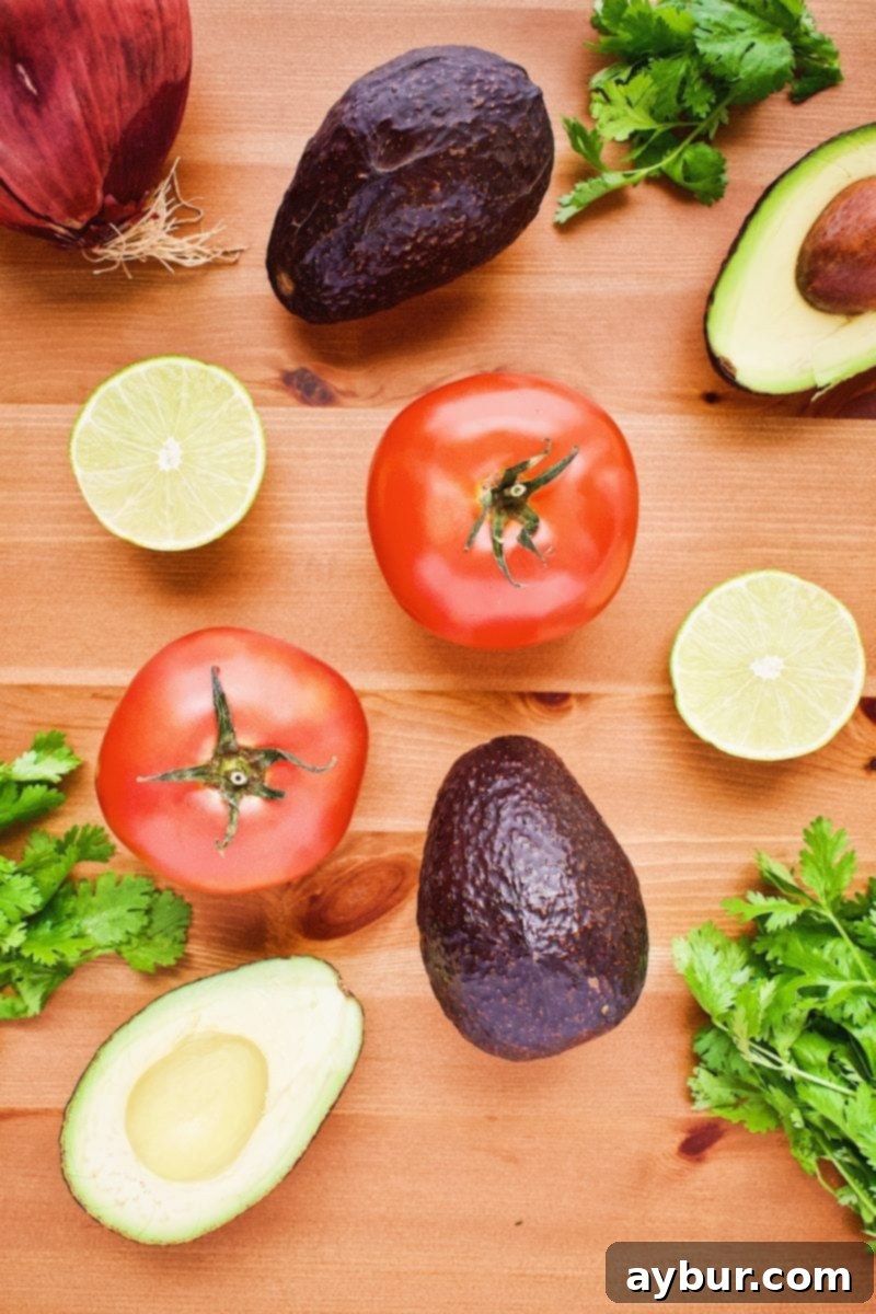 Fresh ingredients for Avocado Salsa laid out on a cutting board, including red onion, tomatoes, avocados, and lime.