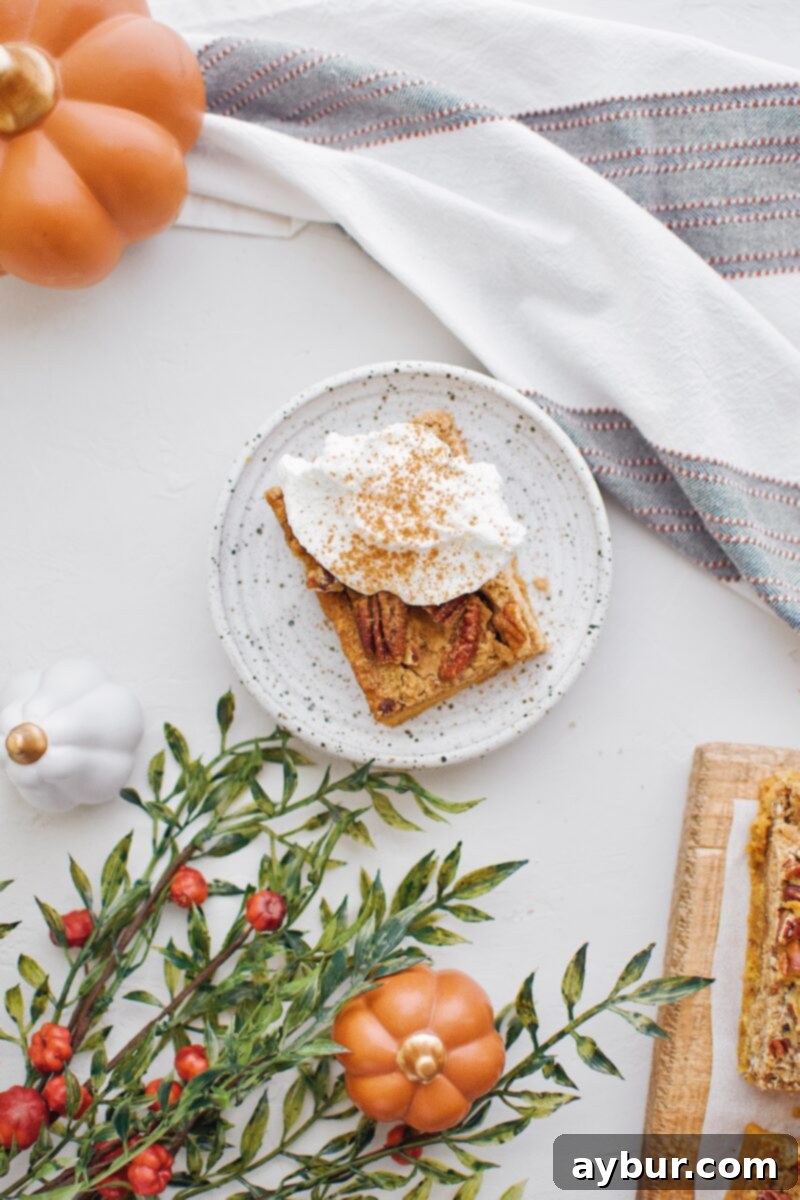 Spiced Pumpkin Bars 6 A close-up of a single Pumpkin Dessert Bar, topped with a generous dollop of whipped cream and a sprinkle of cinnamon, ready to be enjoyed.