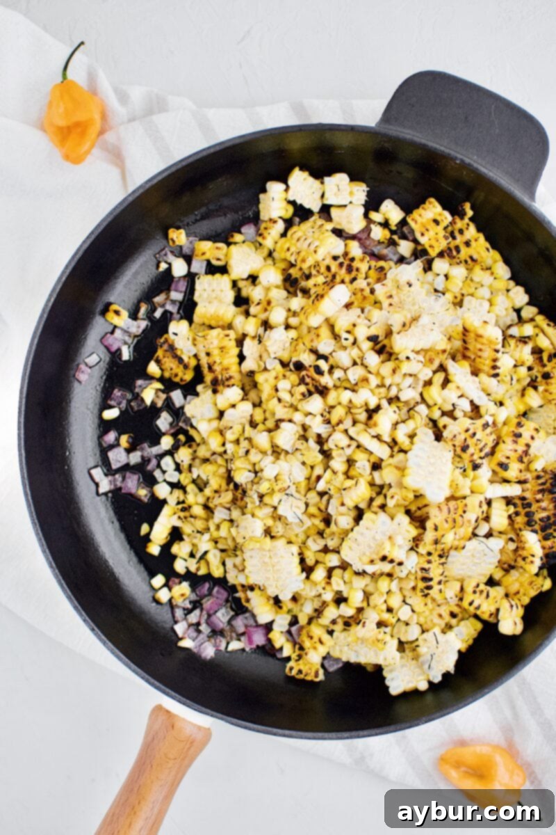 Grilled corn kernels added to the pan with sautéed onions, cooking until warmed