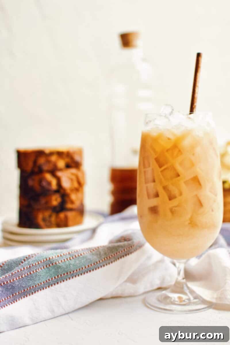 Pumpkin Spice Chai Latte served over ice in a tall glass, garnished with a sprinkle of pumpkin pie spice.