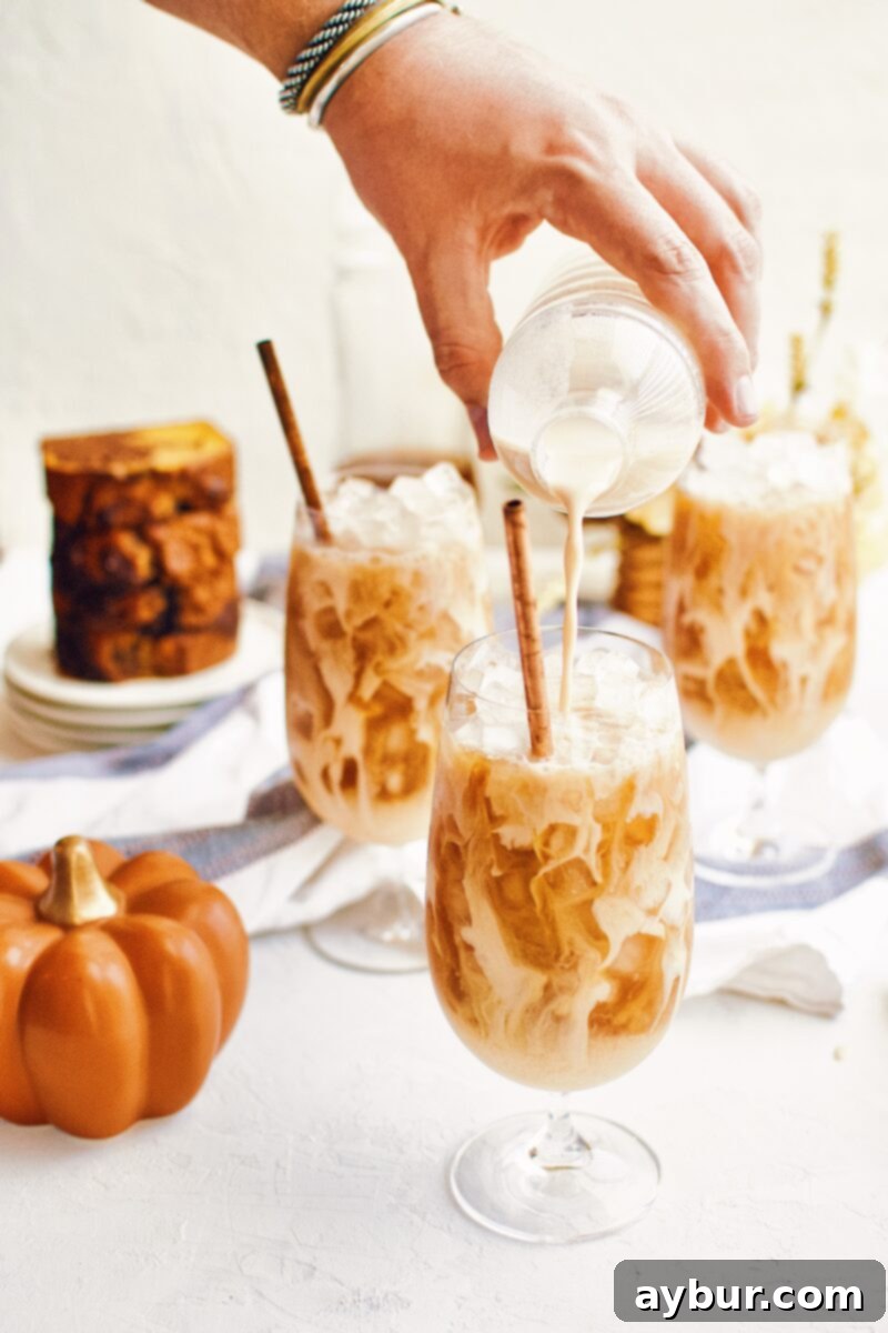 A beautifully layered Pumpkin Spice Chai Latte over ice, garnished with a light sprinkle of spice.