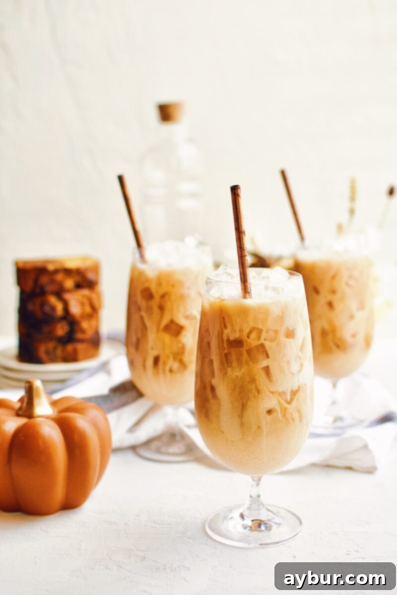 Close-up of a Pumpkin Spice Chai Latte in a glass with ice, showing the creamy texture and spices on top.