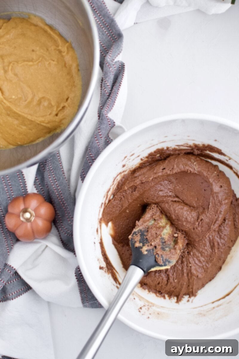 Half of the pumpkin batter removed from the mixing bowl, with cocoa powder being gently folded into the remaining portion to create chocolate batter