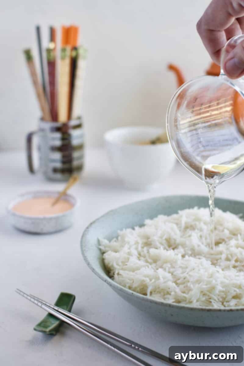 Sushi rice seasoning mixture being poured over warm rice.
