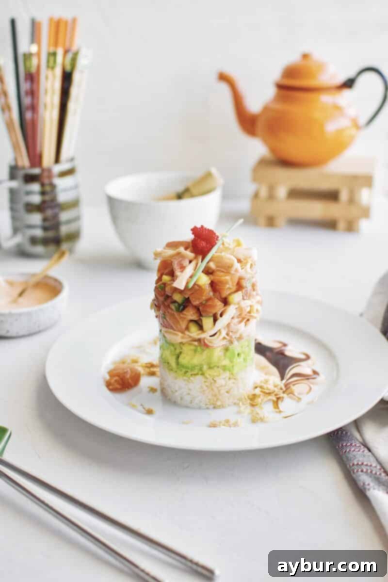 A beautifully presented Spicy Salmon Tower recipe, showing layers of rice, avocado, crab, and salmon.