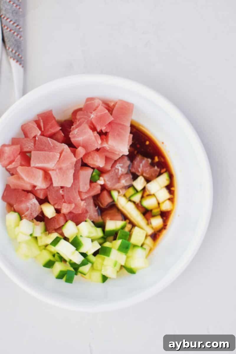 Diced tuna, cucumber, and poke marinade combined in a bowl, ready for marination.