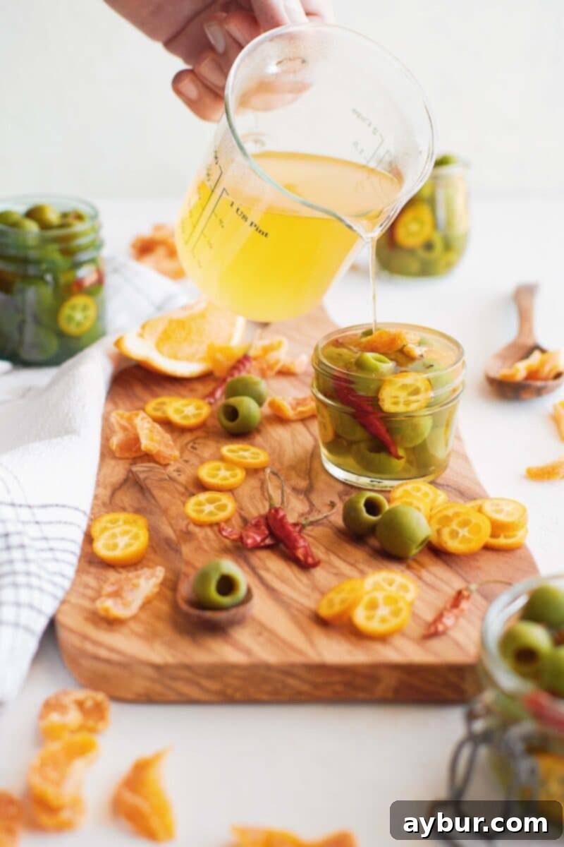 Spicy Citrus Marinated Olives 4 Chef pouring the vibrant brine onto the olives in glass jars