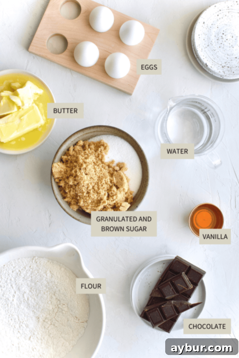 A collection of baking ingredients laid out for a chocolate peanut cake, including butter, eggs, sugars, chocolate, flour, peanut butter, and cream.