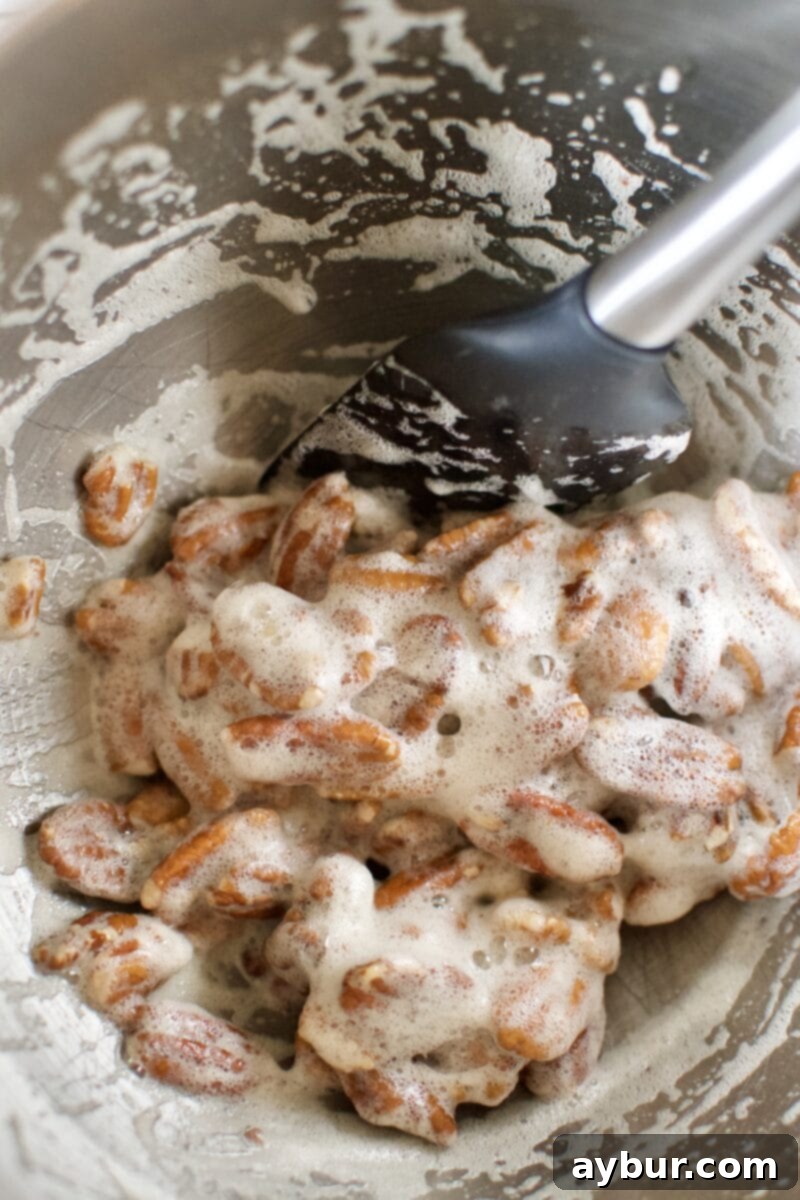 Harvest Pumpkin Spice Pecan Pralines 5 Pecan halves thoroughly coated in the frothy egg white mixture in a mixing bowl.