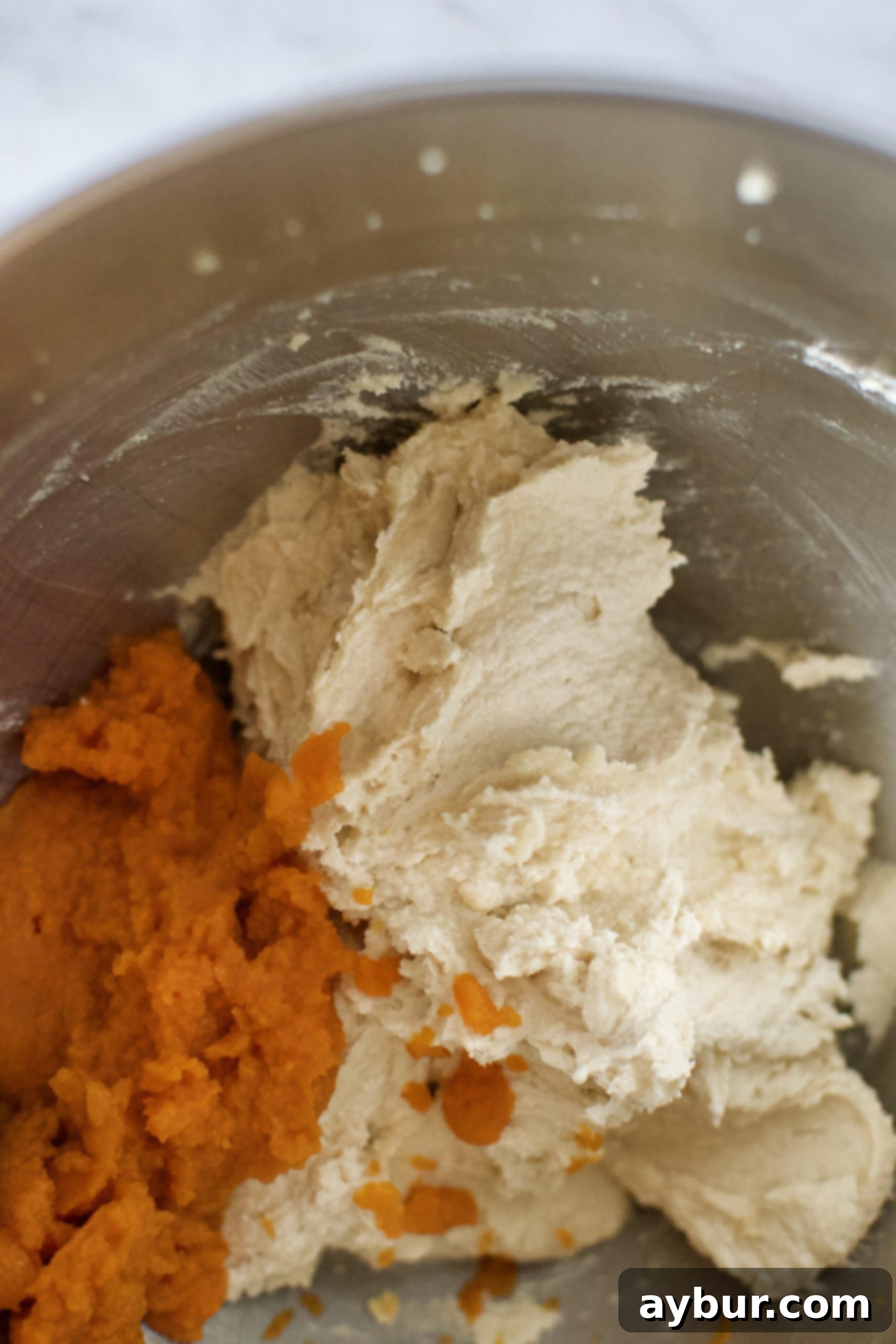 Butter and sugar whipped to a fluffy texture, with pumpkin puree being added into the mixing bowl for the cookie dough.
