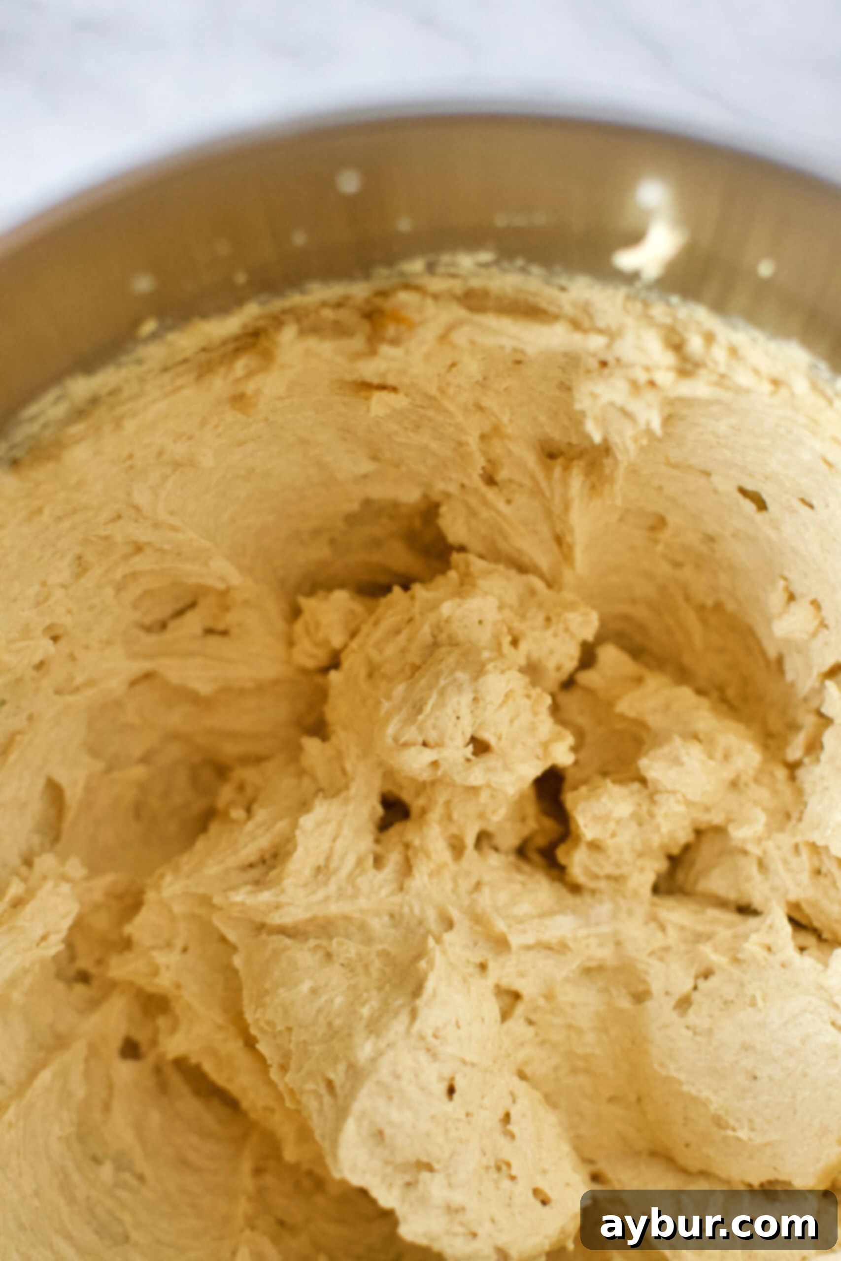 Smooth, orange-colored cookie dough base in a mixing bowl, ready for the addition of dry ingredients and mix-ins.