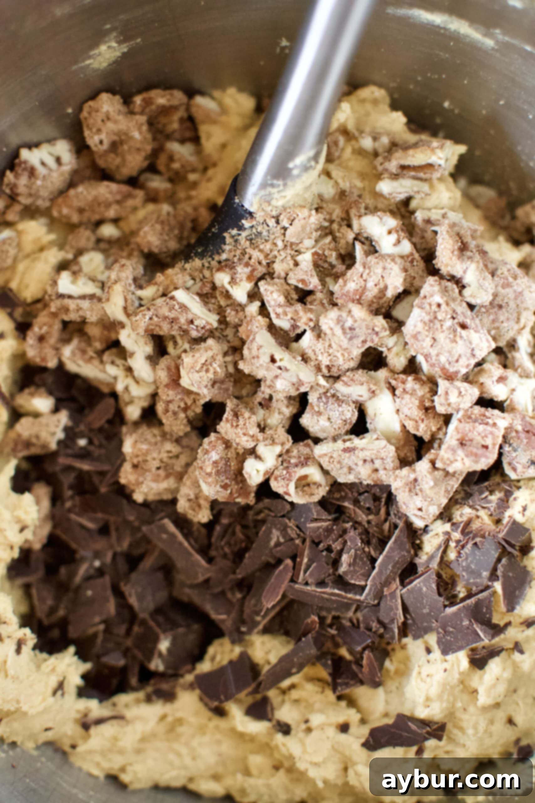 Cookie dough in a bowl with dark chocolate chunks and candied pumpkin spice praline pecans being folded in by hand.