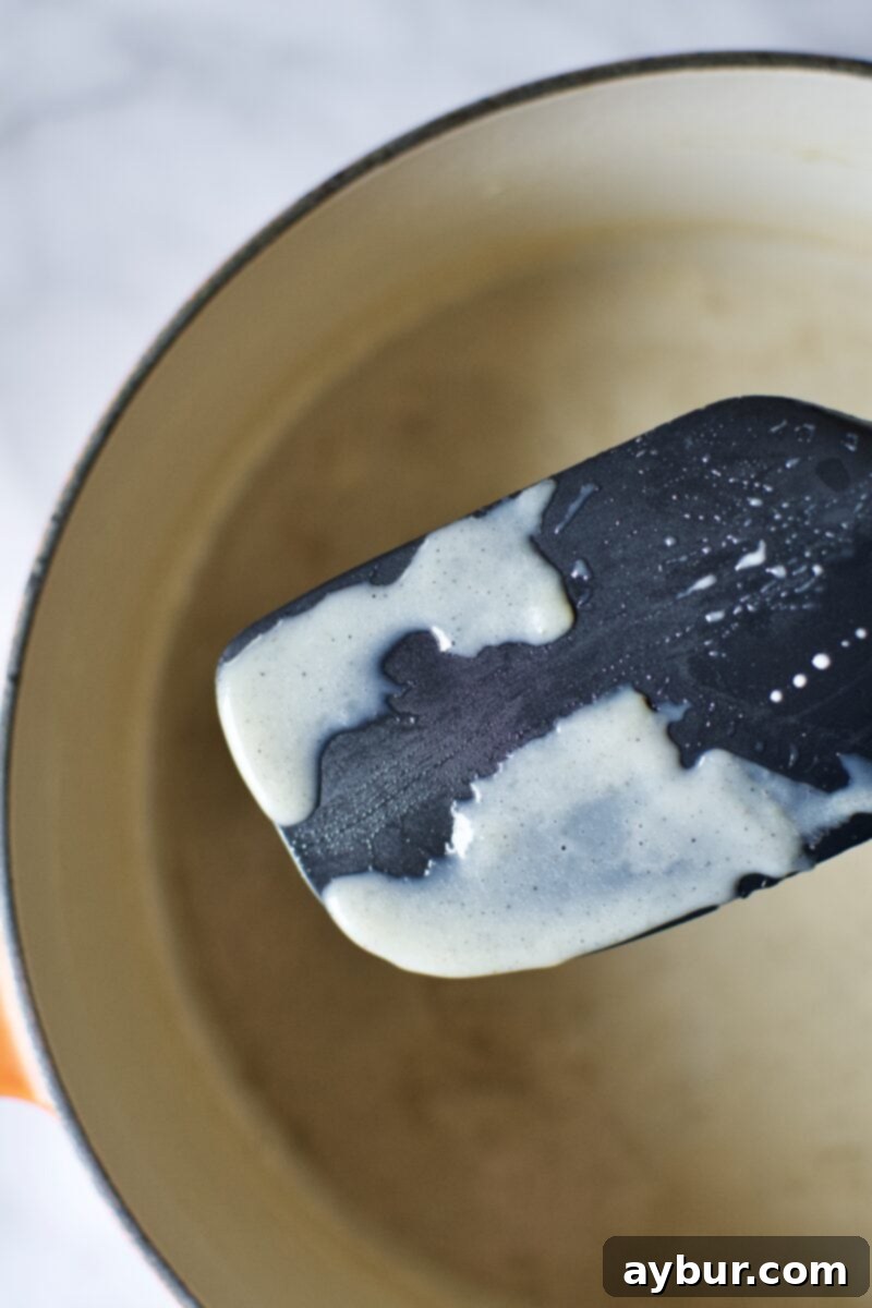 The ice cream base after being cooked until thick, showing it coats the back of a spoon.