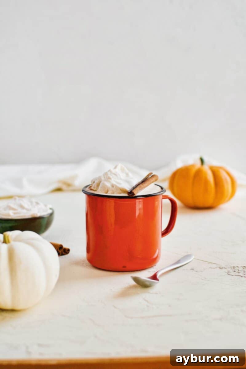 Pumpkin Spice Hot Chocolate in an orange camp mug topped with chai whipped cream and a cinnamon stick, perfectly capturing the essence of fall.
