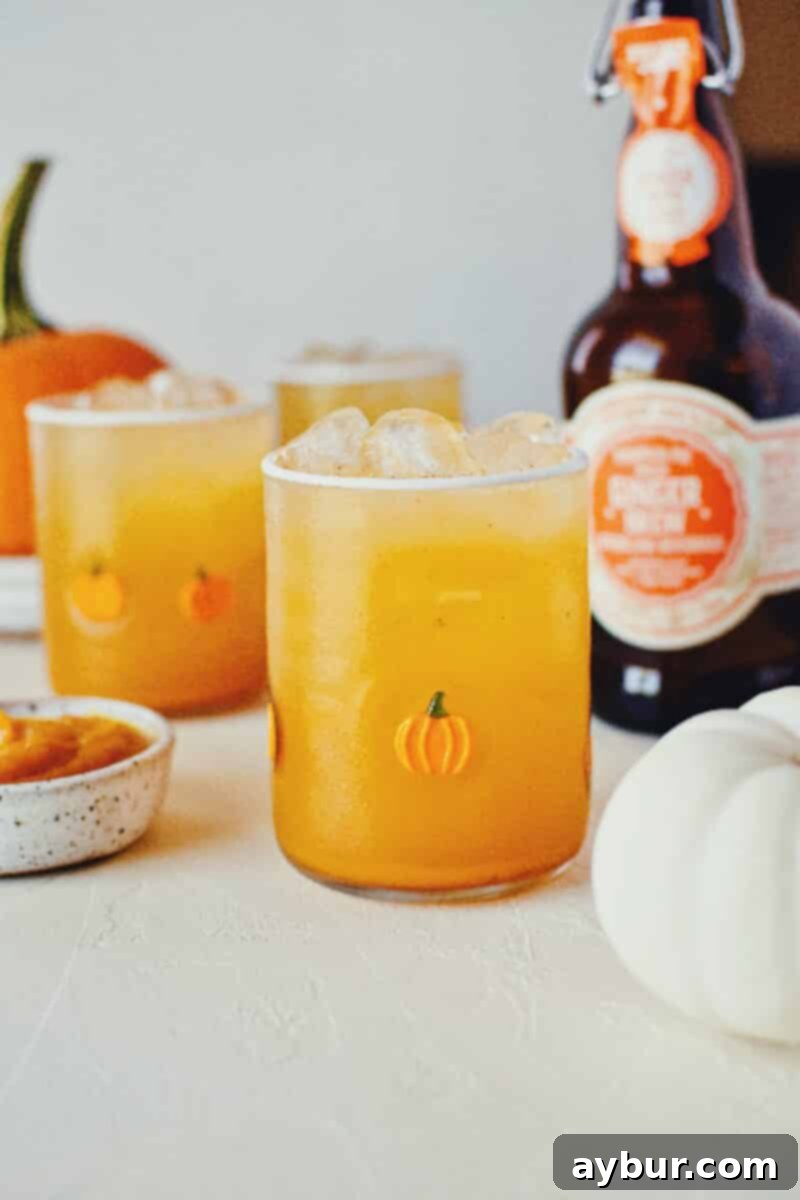 Three glasses of homemade sparkling pumpkin juice, garnished with cinnamon sticks, displayed on a white surface with small pumpkins scattered around.