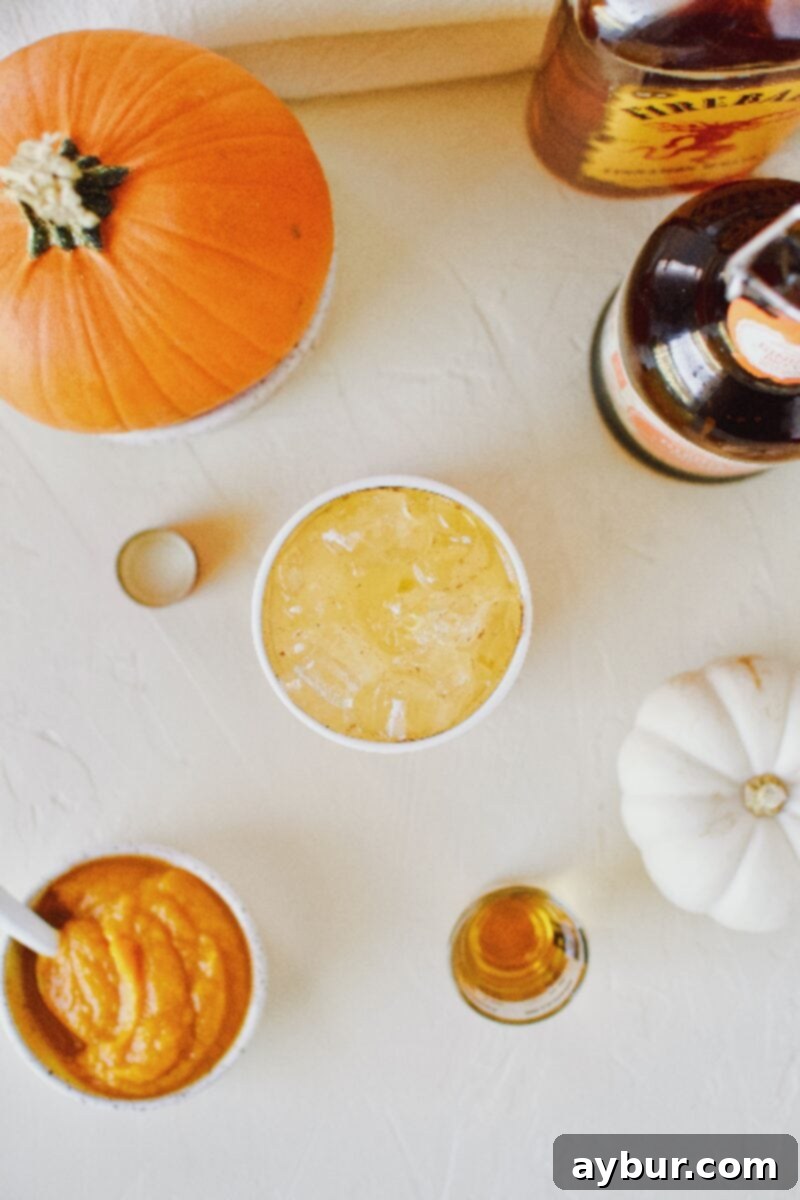 A perfectly garnished glass of spiked sparkling pumpkin juice, with pumpkin spice ginger beer and cinnamon whisky in the background.