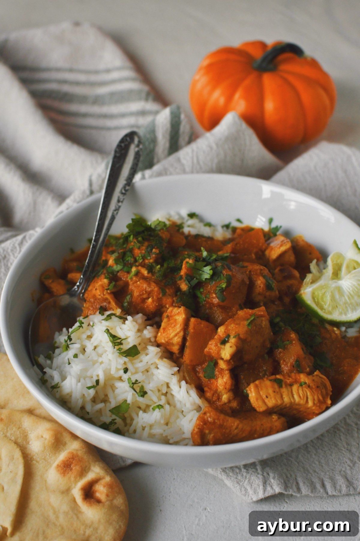 Pumpkin Butter Chicken, with a pumpkin in the background, served over rice and naan bread for dipping.