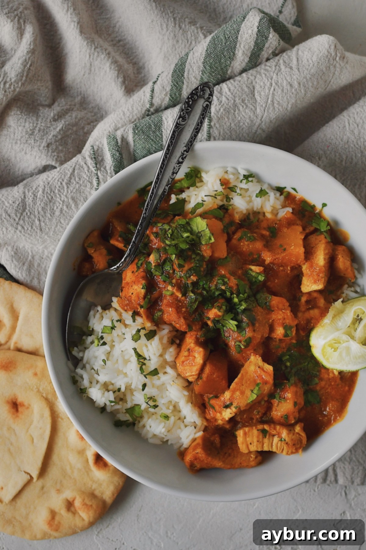 Looking down at a bowl of Pumpkin Butter Chicken served over rice with a lime wedge and cilantro. Some Naan Bread on the side.