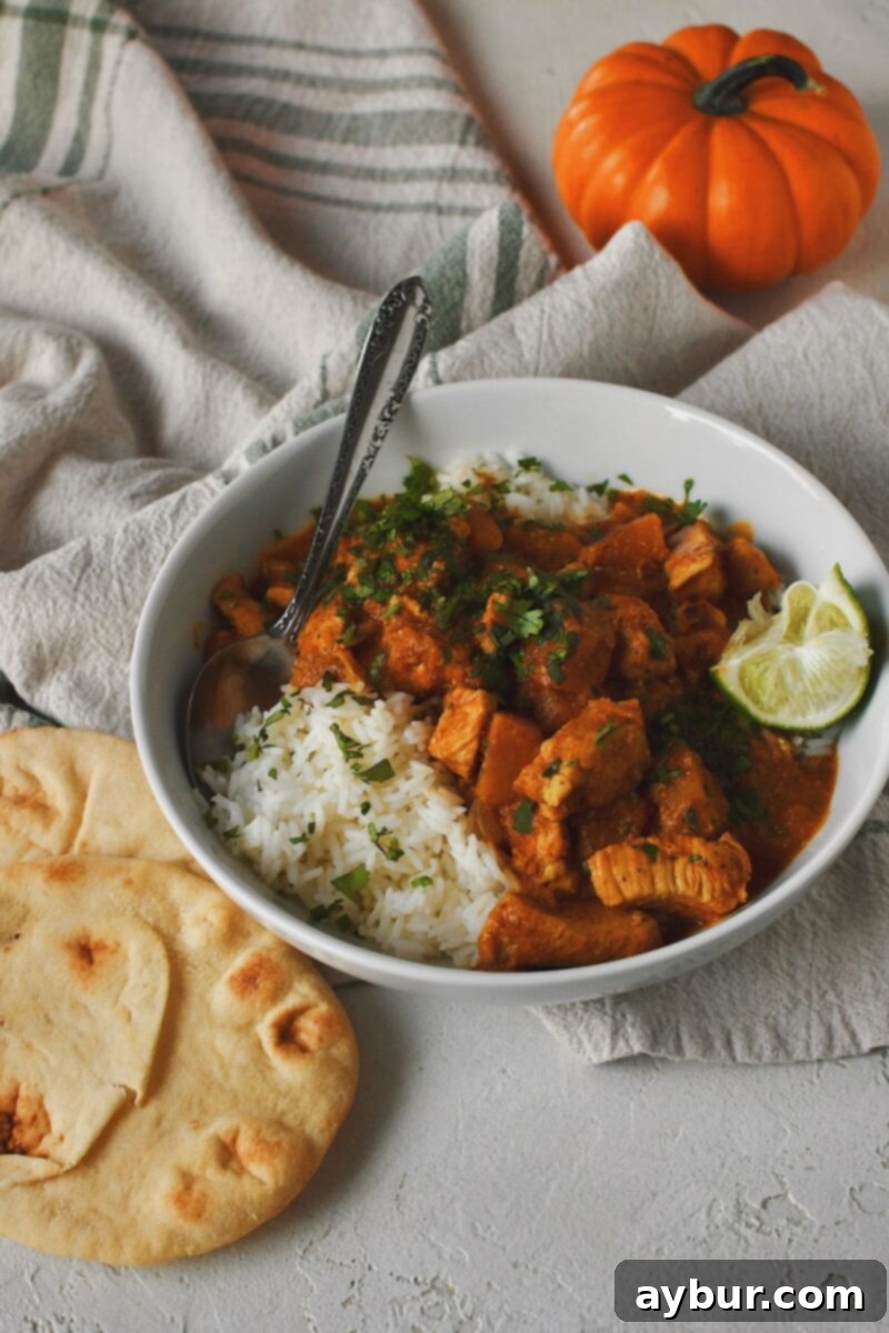 Looking into a bowl of Pumpkin Butter Chicken with a pumpkin in the background and naan bread served on the side.