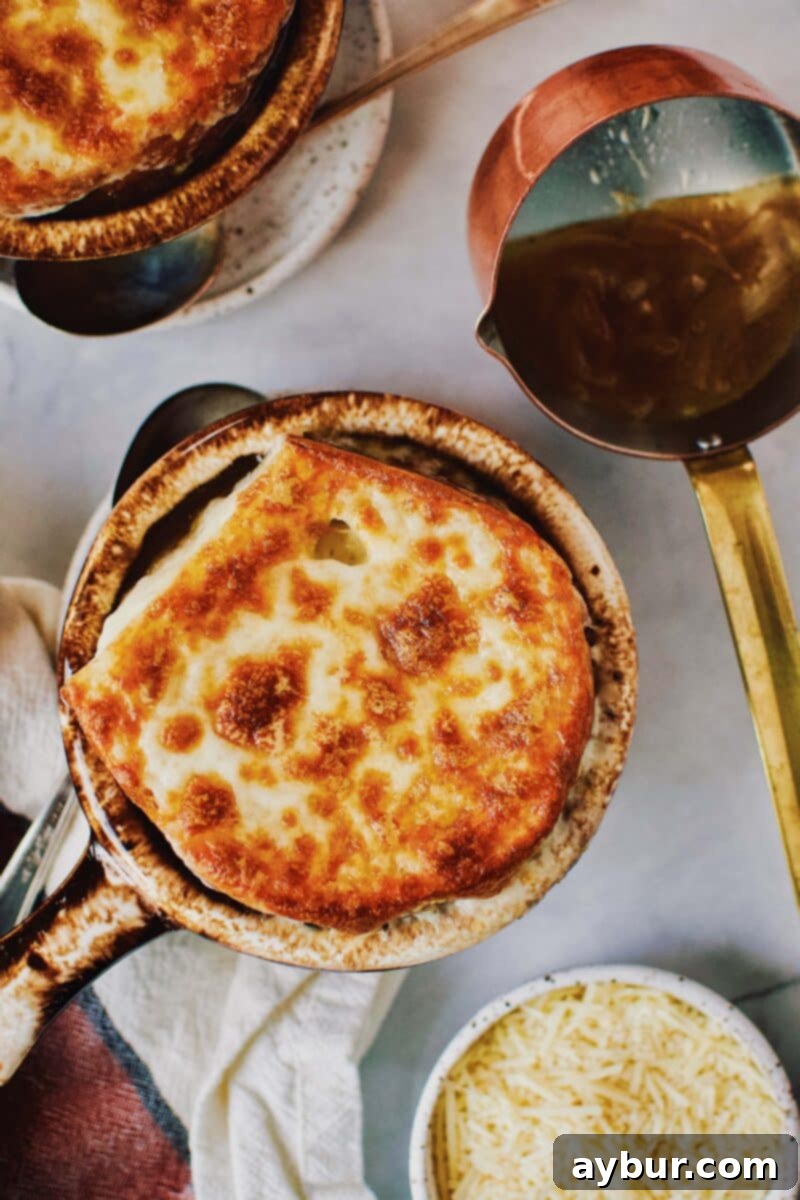 A close-up of a serving of French Onion Soup in a brown crock, topped with a generous layer of melted and browned Parmesan and Provolone cheese over a slice of French bread.