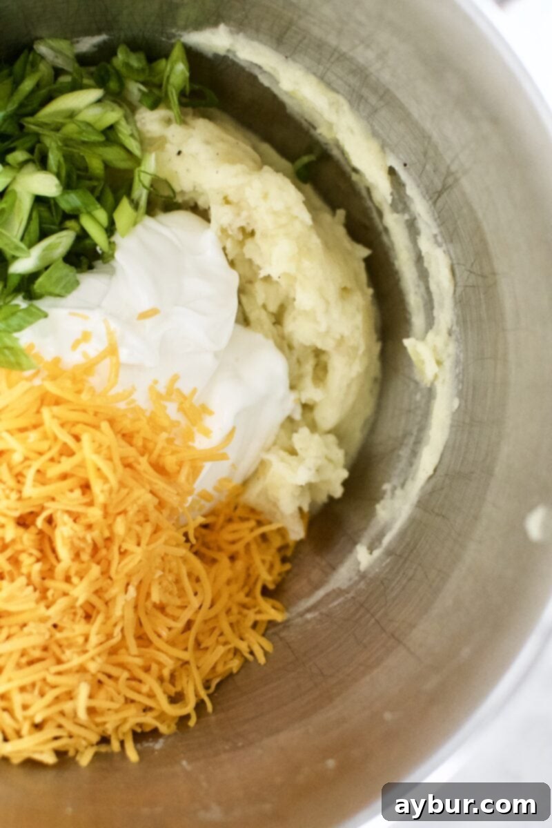 Loaded Baked Potato Mash 6 Sour cream, shredded cheese, and green onions being added to the whipped potatoes in the mixing bowl.
