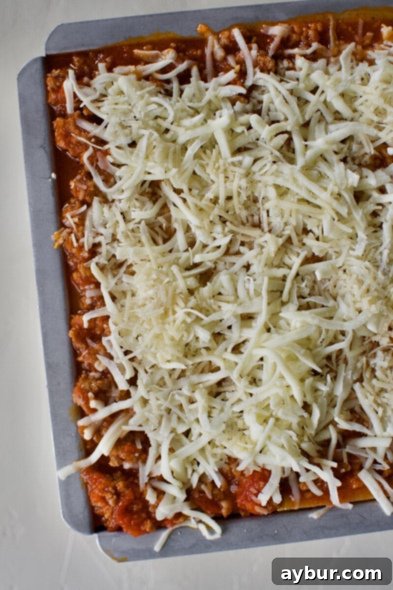 A fully layered homemade lasagna topped generously with a blanket of mozzarella and parmesan cheeses, ready for baking until golden and bubbly.