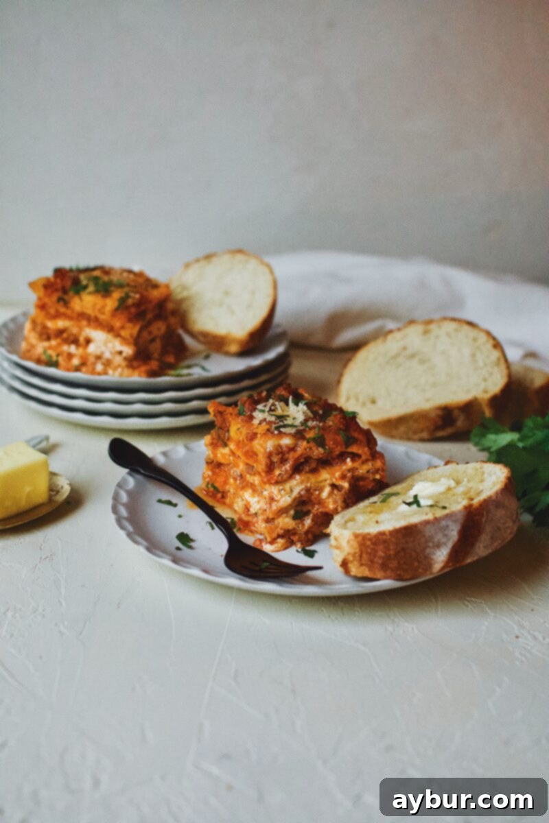 A generous slice of Homemade Lasagna served on a white plate, accompanied by a piece of golden toasted bread with melted butter, showcasing a perfect family meal.