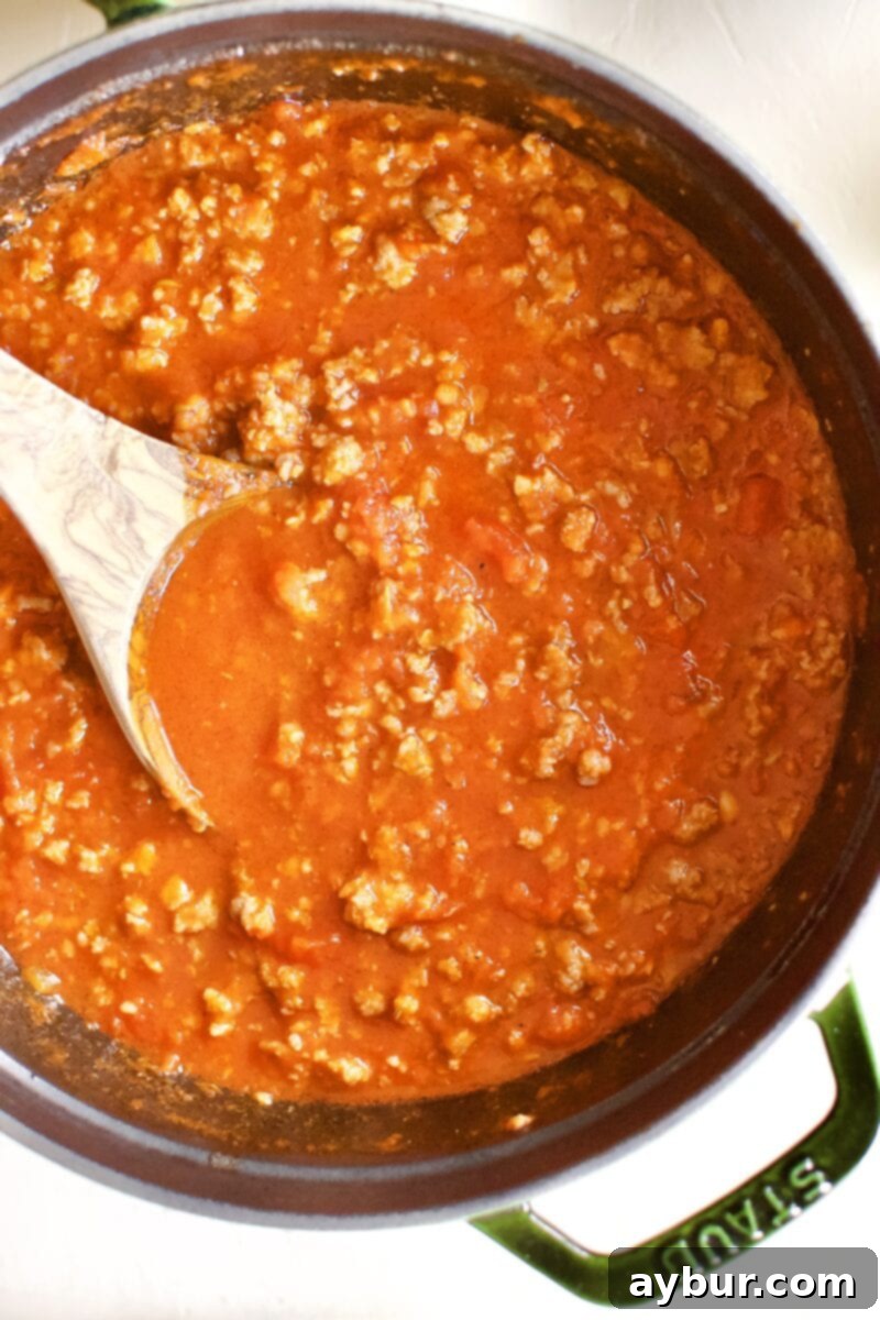 Browned Italian sausage simmering in rich marinara sauce within a large pot, forming the flavorful meat sauce foundation for homemade lasagna.