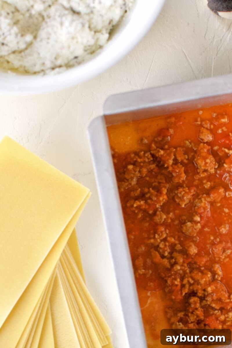 The first foundational layer of homemade lasagna: a generous spread of rich meat sauce covering the bottom of the baking pan.