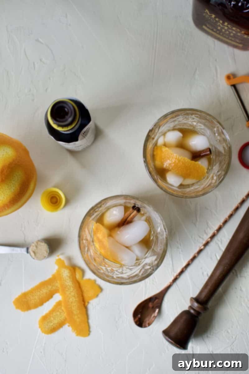 Bourbon whiskey being poured over ice, orange peel, and cinnamon stick in a glass with muddled brown sugar and bitters.