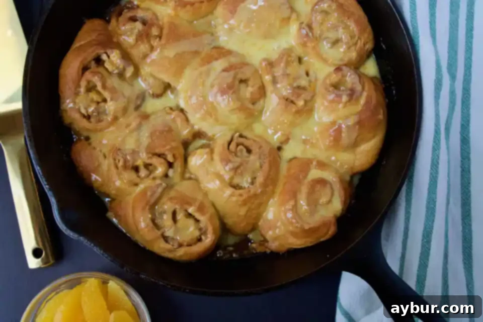 Close-up of golden-brown Quick Orange-Walnut Sweet Rolls, topped with a creamy white glaze and chopped walnuts, showcasing their fluffy texture.