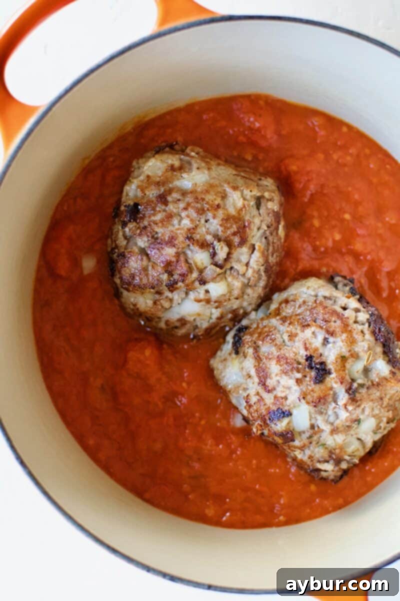 Mega Meatball Masterpiece 11 Perfectly roasted giant meatballs being carefully placed into a pot of simmering tomato sauce.