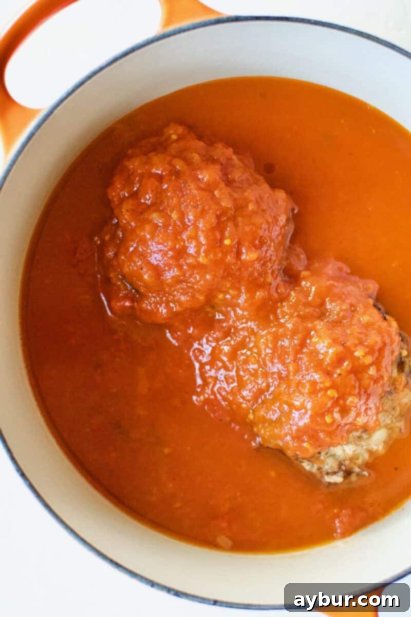 Mega Meatball Masterpiece 12 Generously covering the roasted giant meatballs with rich tomato sauce in a large pot.