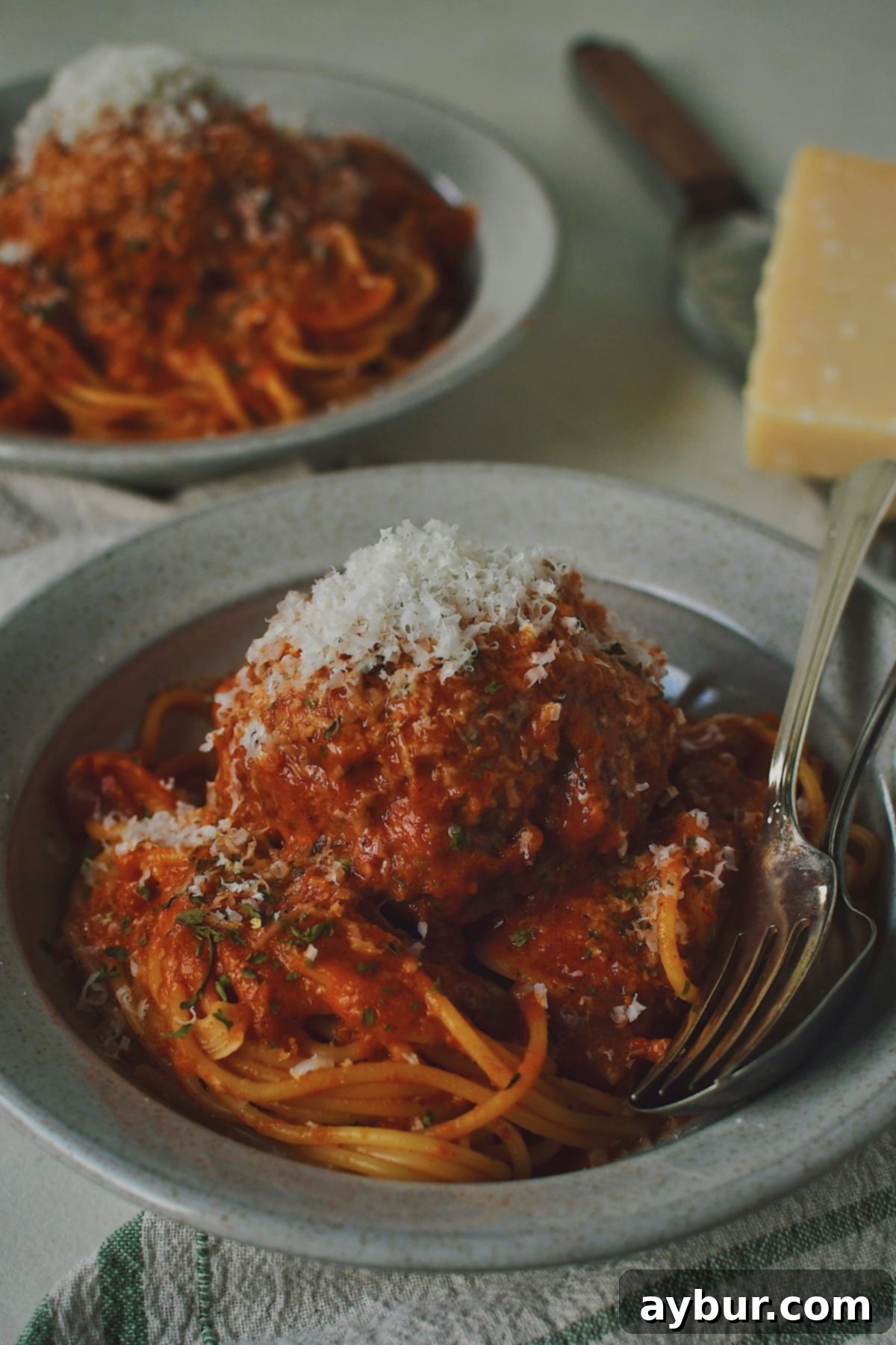 Mega Meatball Masterpiece 13 A delectable close-up of a single giant meatball resting on a mound of spaghetti, beautifully adorned with fresh basil and grated Parmesan.