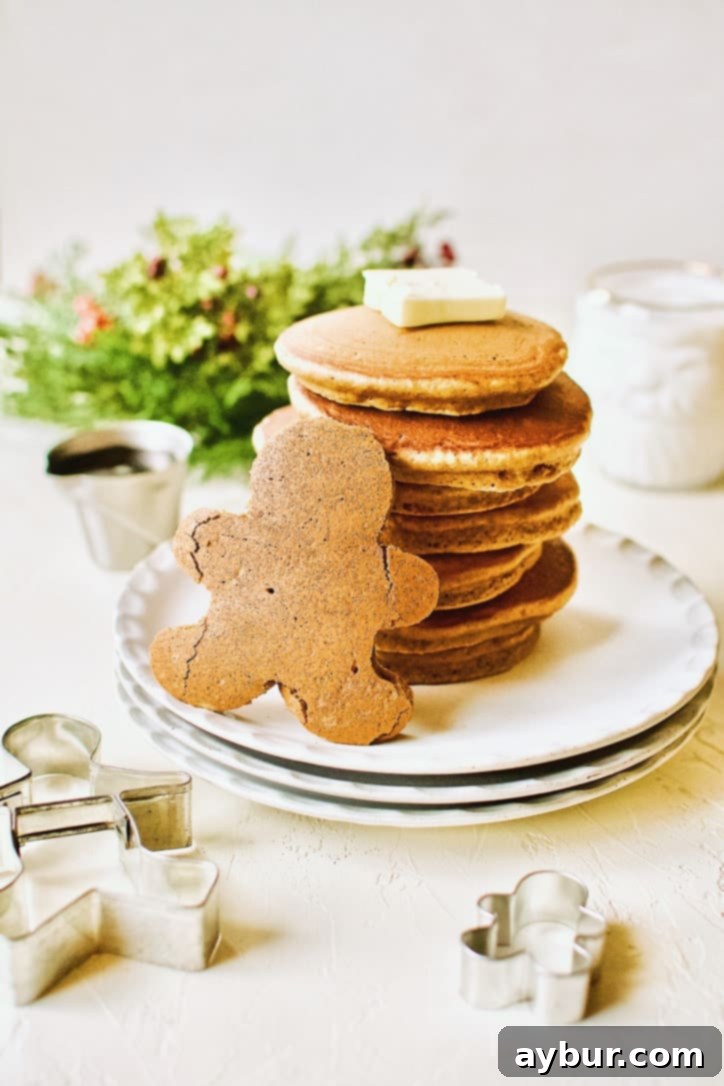 A beautifully arranged stack of golden-brown Gingerbread Pancakes stands tall, proudly accompanied by a gingerbread person-shaped pancake in the foreground, ready for a festive breakfast.
