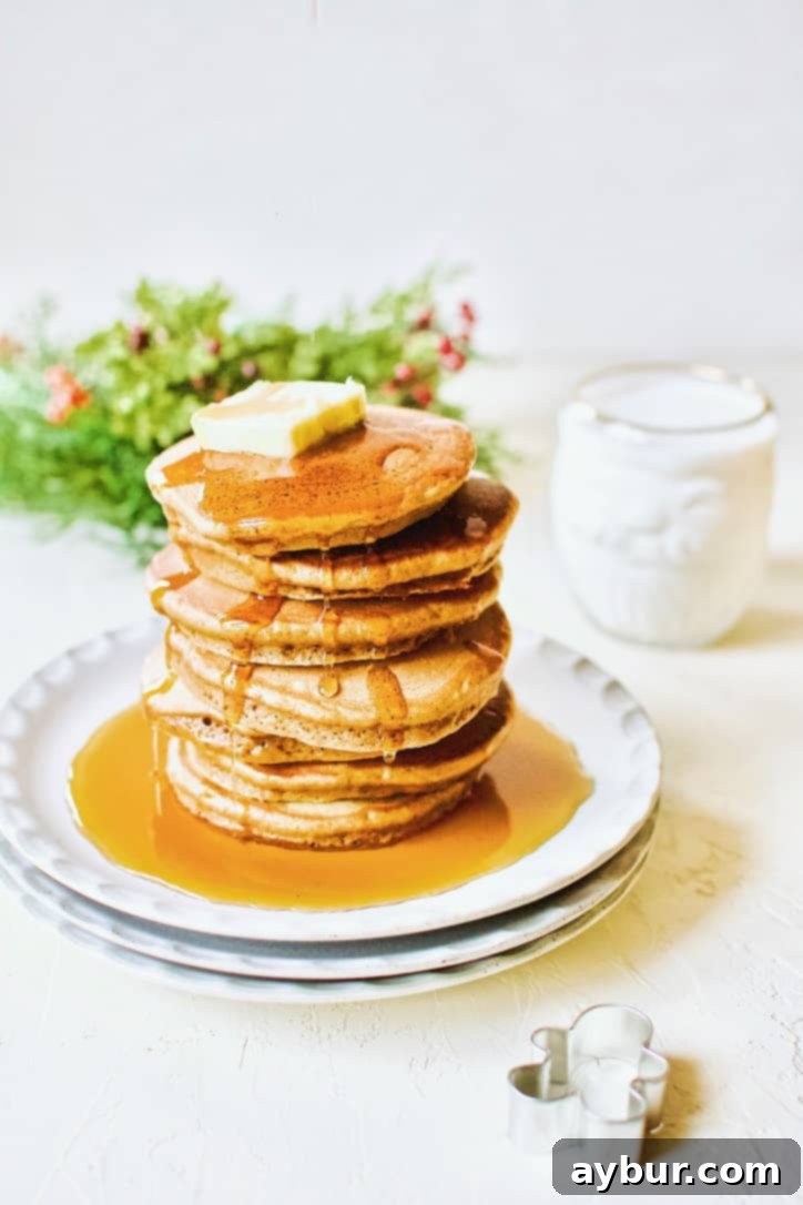 A beautifully decorated stack of Gingerbread Pancakes topped with whipped cream and candied ginger, surrounded by festive holiday decorations.
