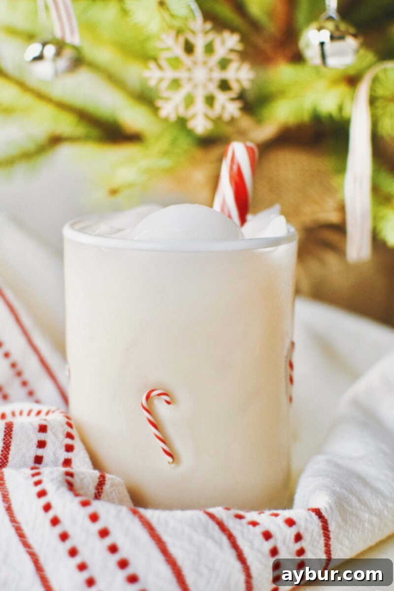 Festive Peppermint Chai Eggnog Cocktail nestled under a twinkling Christmas tree, evoking holiday warmth and cheer.